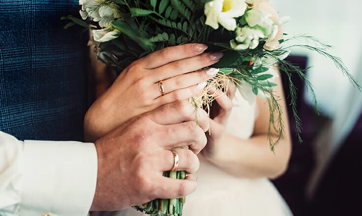 The hands of the bride and groom with wedding rings hold the wedding bouquet